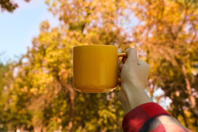 Female hand in shirt hold yellow cup outdoor