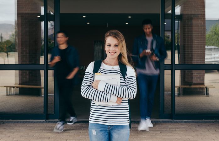 Young woman standing in college with students walking in background in motion blur