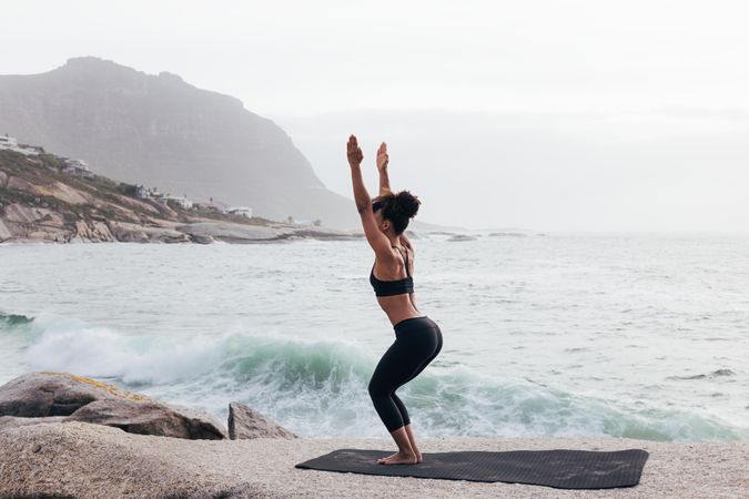 Female stretching doing chair pose next to the ocean