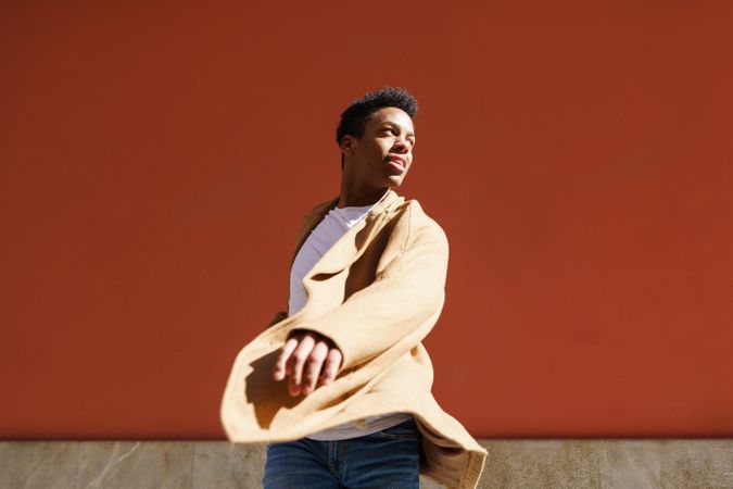 Black male in camel coat with hand towards camera