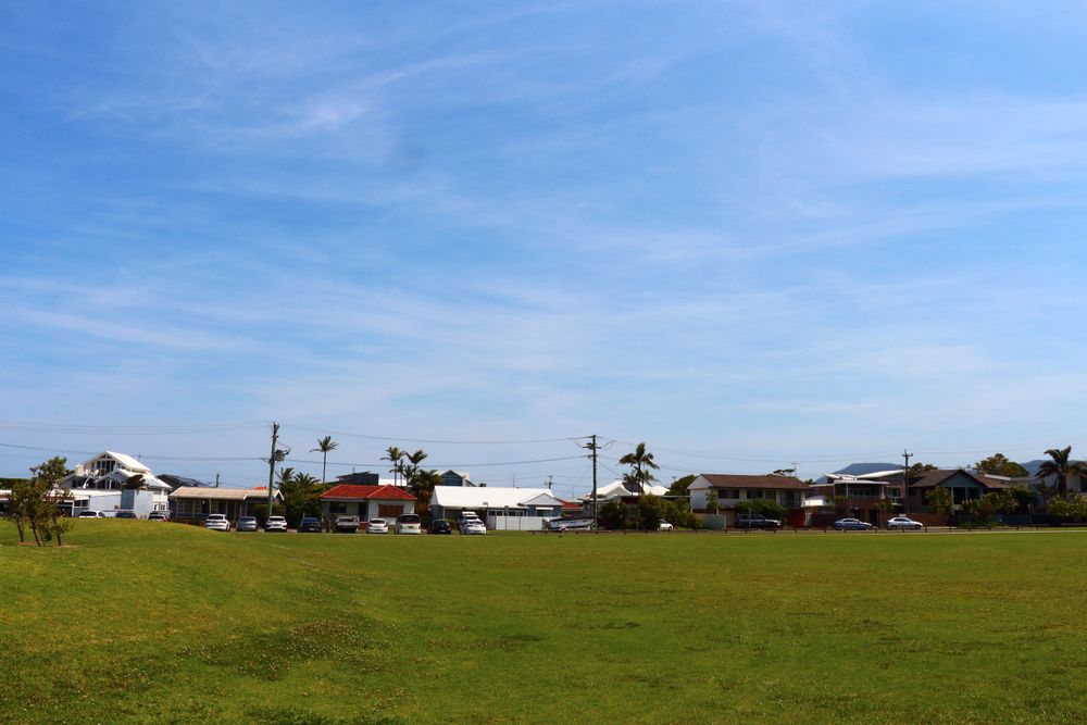 Suburban Houses Next To Open Green Field Under A Clear Blue Sky On A Sunny Day