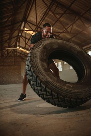 Fit man doing tire flipping workout at empty warehouse