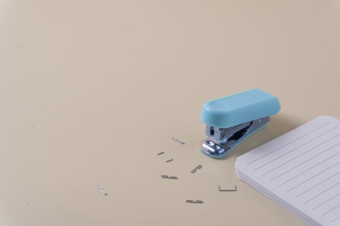 A stapler with scattered staples beside a neat stack of paper ready to be clipped