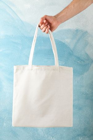 Male hand holding tote bag against blue background, copy space