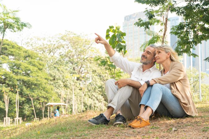 Happy mature man and woman sitting in park and looking up at the trees