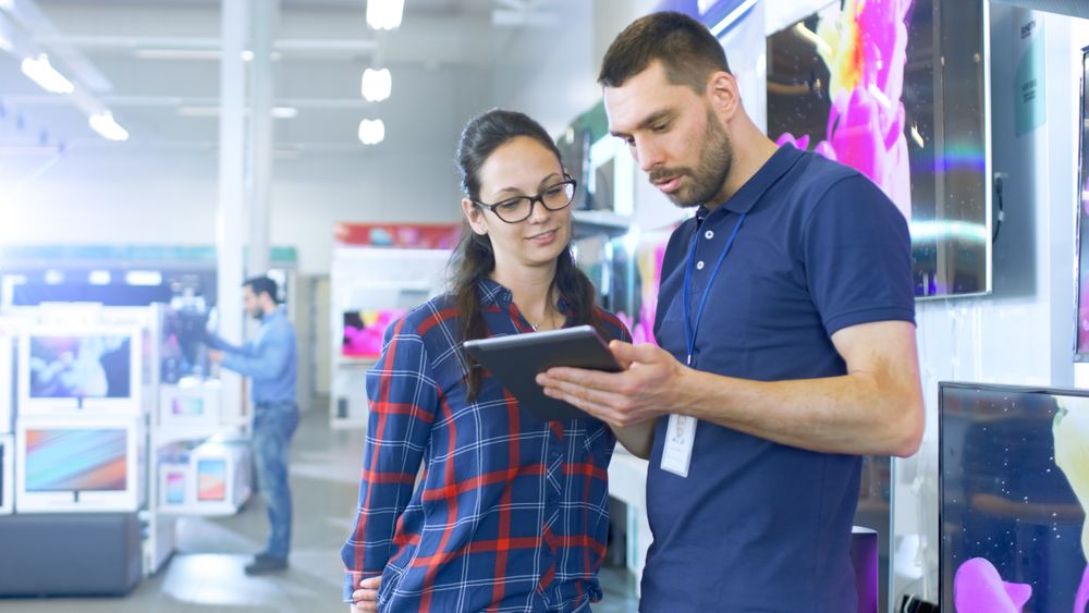 In the Electronics Store Professional Consultant Provides Expert Advice on Tablet Computer Specifications For Young Woman.
