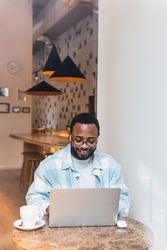 Delighted Black man with coffee browsing laptop