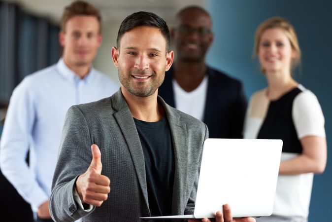 Man with small laptop giving thumbs up in front of his colleagues