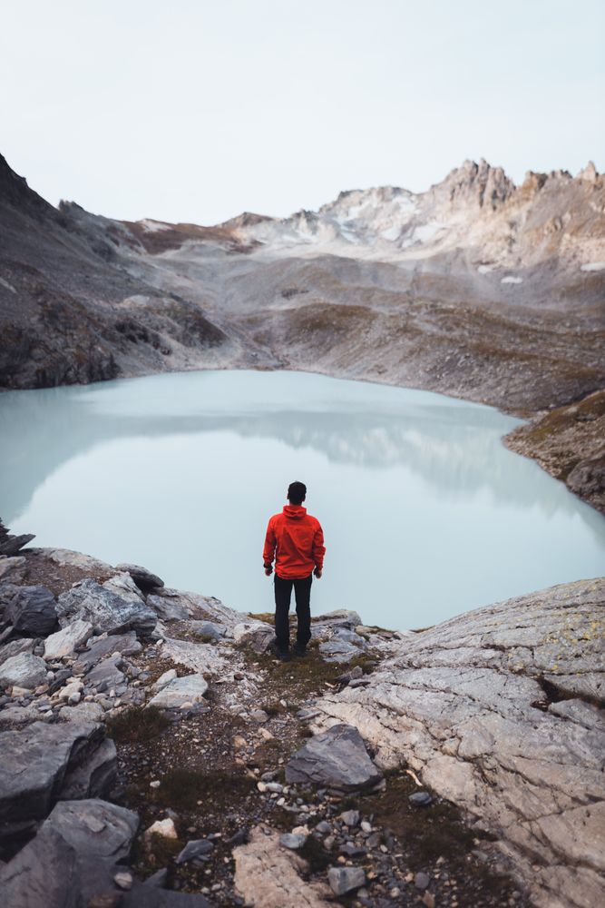Man in red jacket standing on waterside of frozen lake during daytime