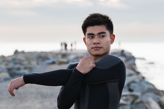 Fit sportsman stretching shoulders near sea