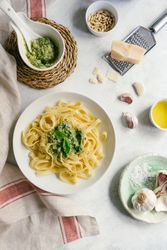 Served plate of pesto pasta next to bowl of sauce on table