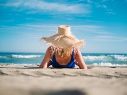 Woman in blue swimsuit and hat on sandy beach