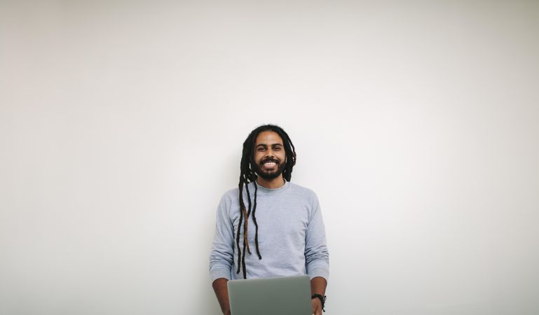 Smiling professional with dreadlocks standing against a light wall