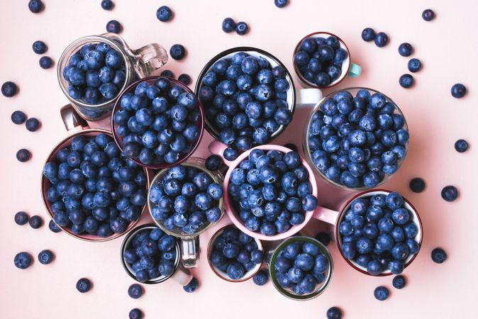 Top view of fresh blueberries in cups on pink background