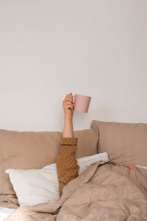 Arm holding coffee mug in bed