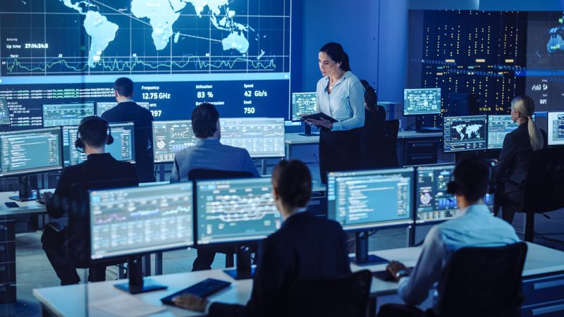 Diverse Team in a High-tech Control Room Monitors Global Data on Multiple Screens
