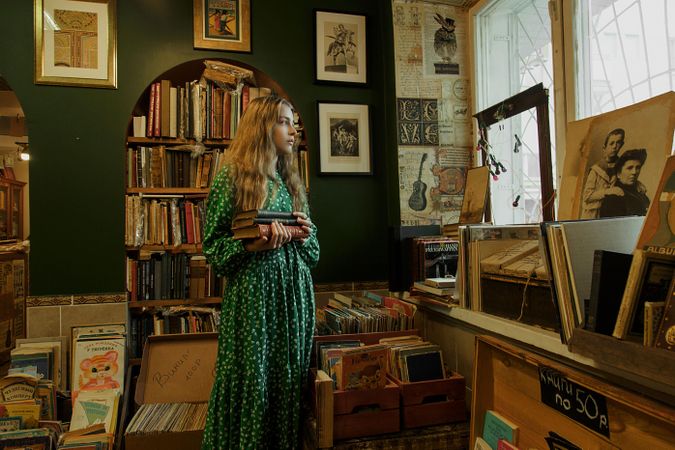 Girl holding books and standing in a room filled with books and music records