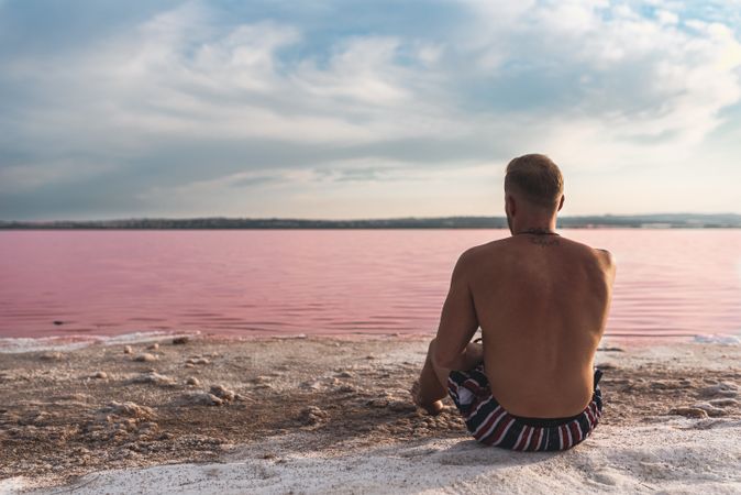 Tranquil man in swimwear sunbathing on shore of pink lake