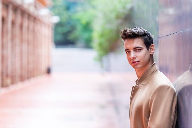 Young man leaning on wall outside looking at camera