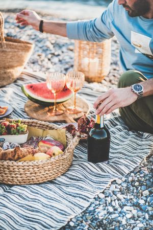 Man with hand on bottle of wine at outdoor picnic