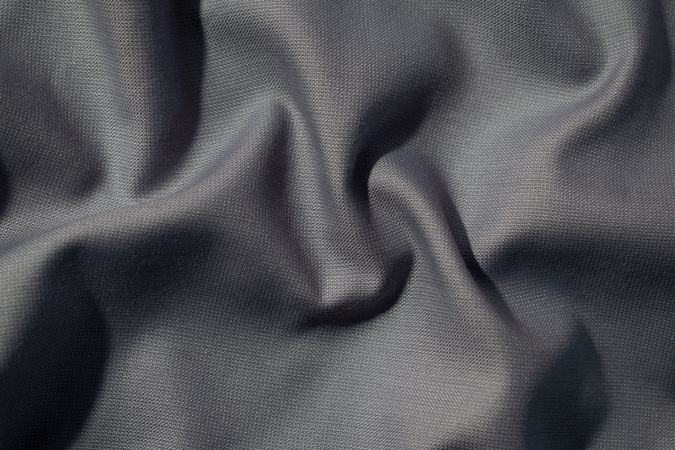 Crumpled wavy dark grey silky fabric background texture. siny and glossy.