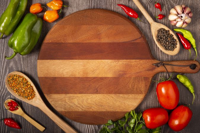 Empty pizza  board on the table with Ingredients for cooking. Tomatoes, various peppers, garlic and green peppers.