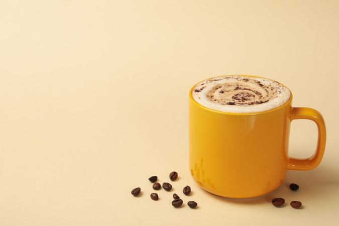 Cup of latte and coffee seeds on beige background
