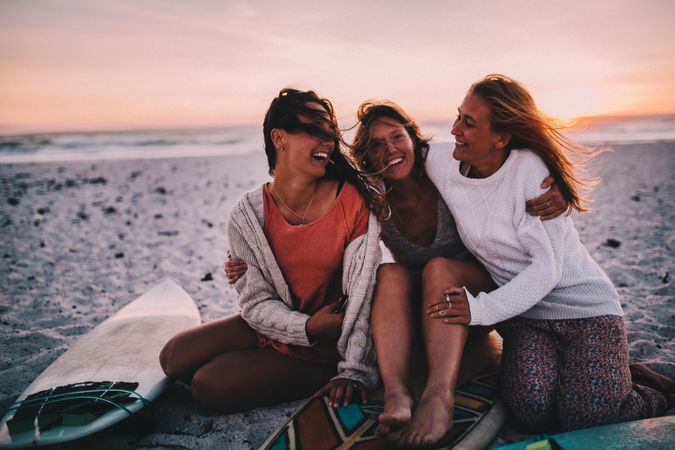 Group of young women sitting on the sand at the beach at sunset smiling