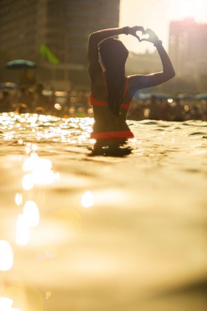 Anonymous woman standing in sea and gesturing heart