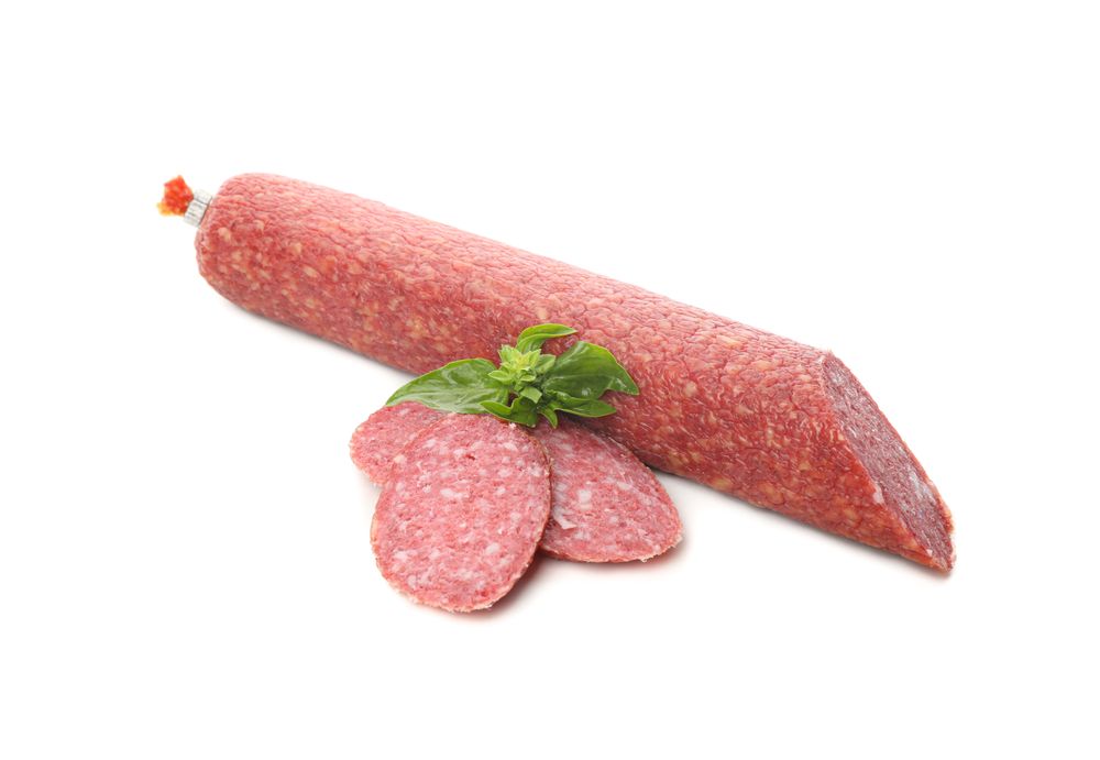Salami stick with slices and basil in plain room