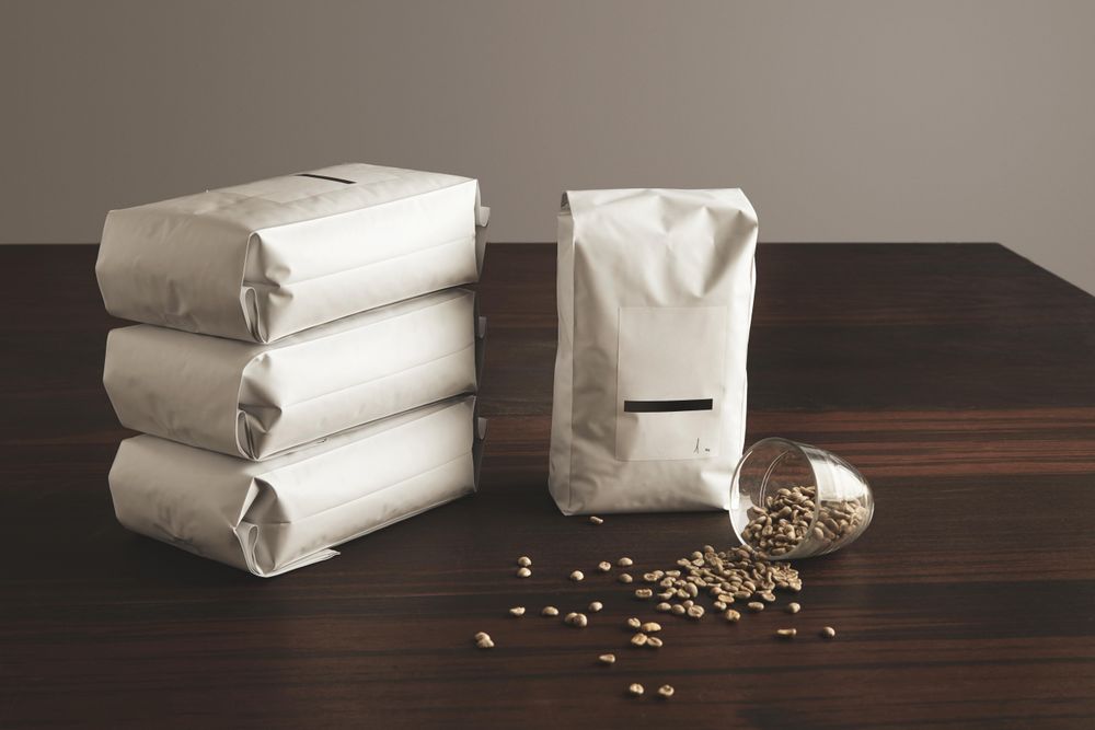 Pouches of coffee beans with blank label with spilled glass of whole beans