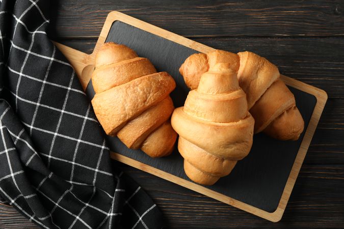 Bread board with croissants on table with kitchen towel, top view