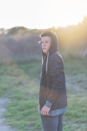 Teenage male in hoodie and eyewear standing in field