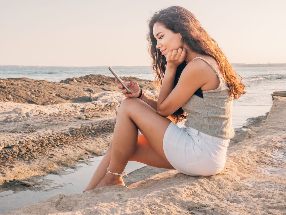 Dreamy trendy young woman texting on beach