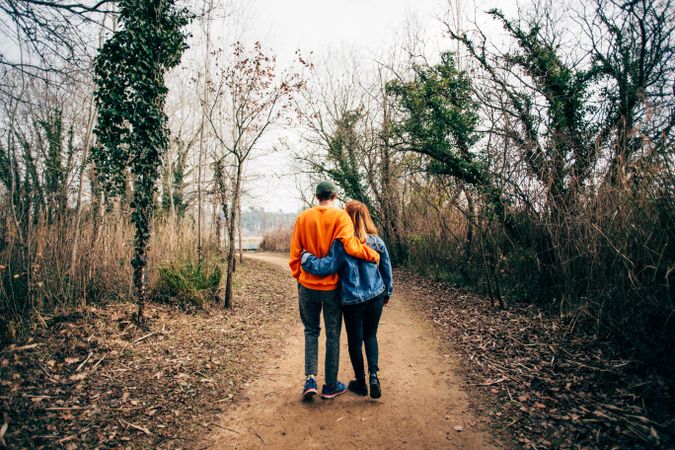 Man and woman with their arms around each other walking through the woods