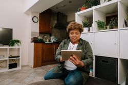 Older Black woman sitting on sofa using tablet