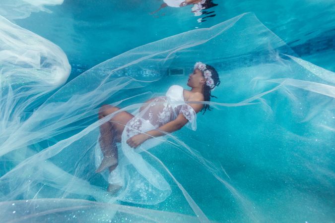 Pregnant woman in wreath and dress underwater