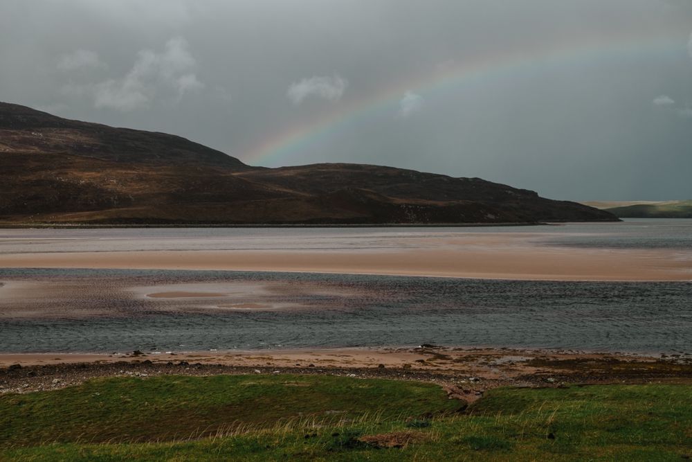 Dim rainbow over Scottish coast at sunset