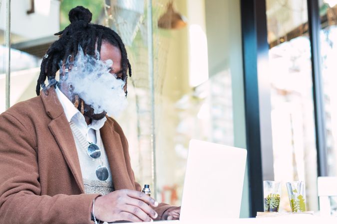 Smoking Black man using laptop on restaurant terrace