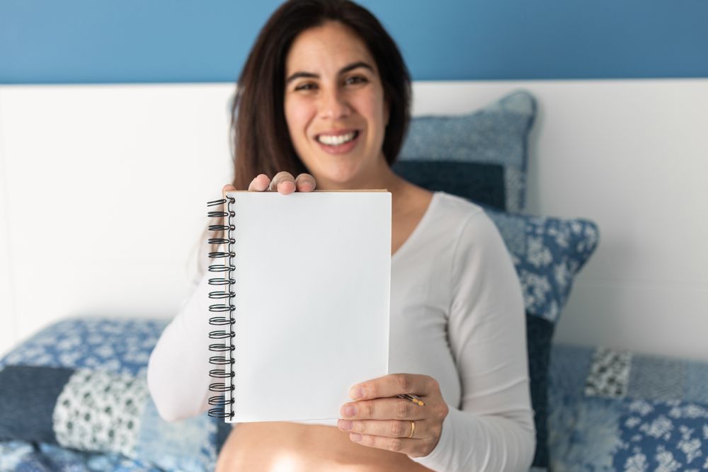 Cheerful pregnant woman showing notebook at camera
