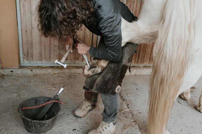 Man shoeing horse near stable