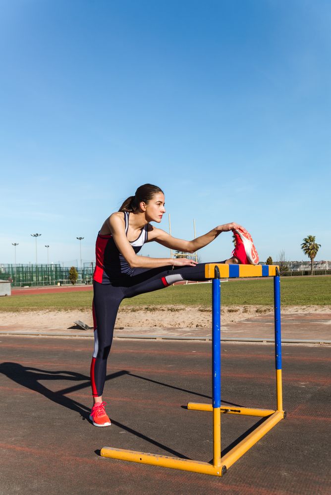 Female athlete stretching on hurdle on stadium