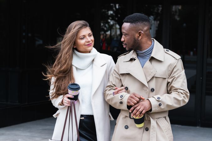 Happy multiethnic couple in stylish clothes with takeaway coffee