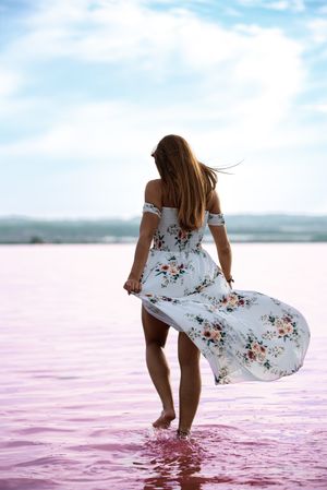 Peaceful woman in white dress walking ankle deep in pink lake