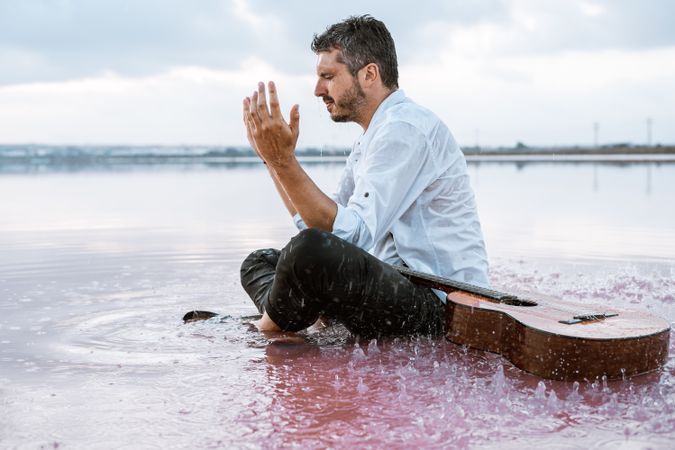 Musician with guitar on pink sandy water