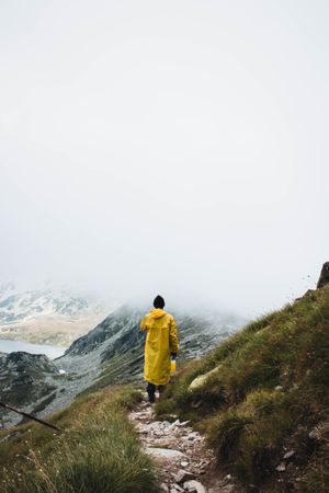 Back view of a person in yellow raincoat standing on top of a mountain