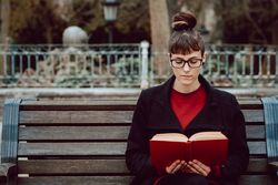 Young woman reading book on bench in park