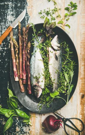 Sea bass with herbs and purple asparagus in dark bowl, with knife and onion vertical composition