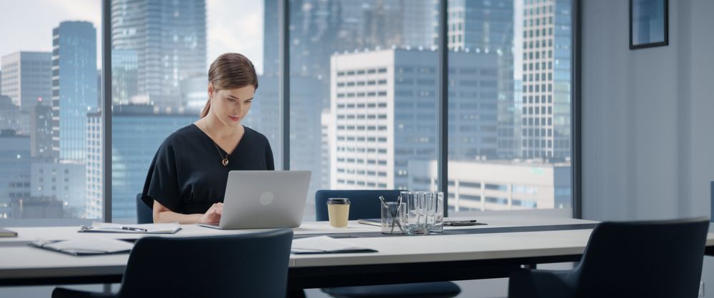 Portrait of Successful Businesswoman Working on Laptop Computer in Her Big City Corner Office.