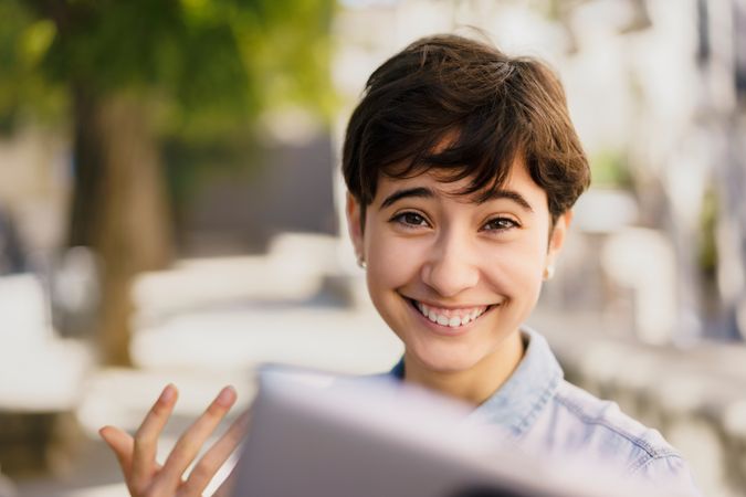 A smiling young woman enthusiastically engaging with a tablet in a cheerful outdoor setting